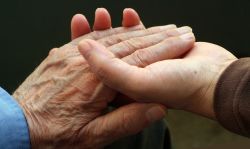 Junge Frauenhände umfassen die Hand eines alten Mannes