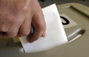 Eine Hand steckt einen Zettel in eine Wahlurne.