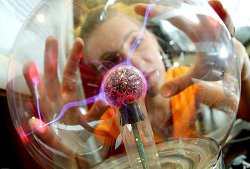 Eine junge Frau schaut sich eine mit Plasma gefüllte Glaskugel an, in der sich mittels hochfrequenter Spannung farbige Lichtblitze erzeugen lassen.