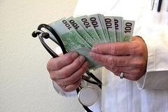 Ein Arzt hlt ein Stetoskop sowie etliche 100-Euro-Scheine in der Hand.