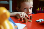 Junge sitzt an einem roten Tisch und zählt sein gespartes Taschengeld - Video ansehen... - Öffnet neues Fenster