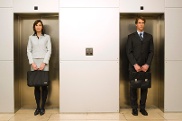 Eine Frau und ein Mann stehen nebeneinander, jeder vor einer verschlossenen Aufzugstür.