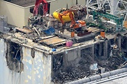 Eine Luftaufnahme auf den zerstörten Reaktor von Fukushima. Auf dem Dach stehen schwere Maschinen, ein Bagger und ein Kran.