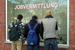 Drei Jugendliche stehen vor einem Fenster der Agentur für Arbeit, auf dem das Wort Jobvermittlung steht.