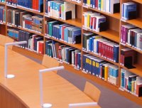 Foto: Lesesaal der Bibliothek, im Vordergrund Schreibtisch mit Stuhl und Leselampe, im Hintergrund Regal mit vielen Büchern