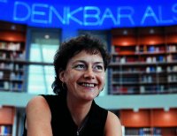 Foto: Portrait einer Mitarbeiterin der Bibliothek, im Hintergrund Regale mit Büchern