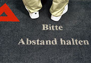 Bild: Auf dem Teppich befindet sich neben dem Arbeitsamtslogo der Hinweis „Bitte Abstand halten“.