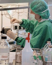 Bild: Die Mitarbeiterin hat grüne Laborkleidung an und trägt Handschuhe