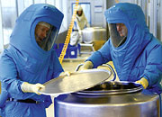 Bild: Zwei Männer in blauen Schutzanzügen öffnen einen Behälter