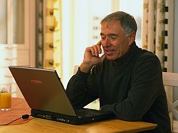 Mann sitzt hinter einem Laptop und telefoniert per Mobiltelefon