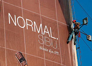 Ein Kletterer bringt an einer Hauswand ein Riesenposter mit der Aufschrift "Normal. Sibiu." an.