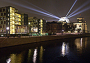 Bild: Die leuchtende Reichstagskuppel bei Nacht. Lichtstrahlen sind in den Himmel gerichtet.