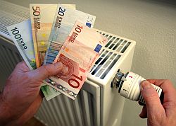 Eine Hand hält in einer Wohnung Geldscheine vor einen Heizkörper