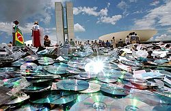 Eine Menschenmenge steht am 3.12.2003 vor dem Nationalkongress in Brasilia neben einem großen Berg an CDs. Die mehr als 500.000 Raubkopien sollen mit einer Straßenwalze vernichtet werden.