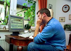 Junger Mann sitzt Zuhause vor seinem Computer, Klick vergrößert Bild