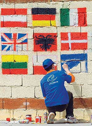 Jugendlicher gestaltet eine Wand mit Flaggen europäischer Länder.