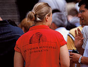 Eine Mitarbeiterin vom Besucherdienst. Sie trägt ein rotes T-Shirt mit einem Logo der Kuppel auf dem Rücken.