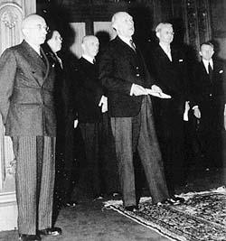 Fotografie: Bundeskanzler Konrad Adenauer steht auf dem Teppich, der nur für die Hohen Kommissare vorgesehen war. Hinter ihm Mitglieder der ersten Bundesregierung.
