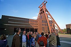 Besuchergruppe steht vor dem Doppelbock-Fördergerüst des Schachts XII der Essener Zeche Zollverein.