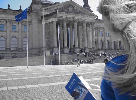 Ein junge Frau steht mit dem Grundgesetz in der Hand vor dem Reichstagsgebäude.