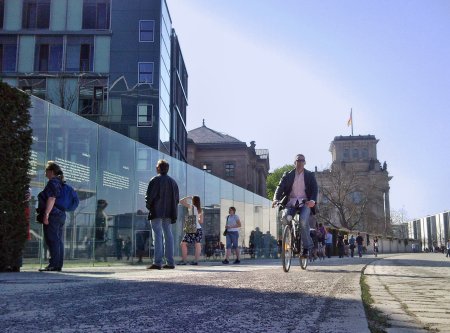 Glaswand mit dem Grundgesetz im Regierungsviertel, Leute lesen die Artikel, ein Radfahrer fährt vorbei.
