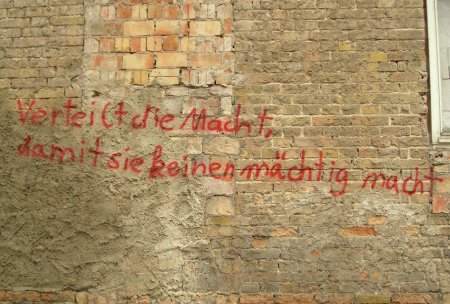 Roter Schriftzug auf einer Mauerwand: Verteilt die Macht, damit sie keinen möchtig macht.