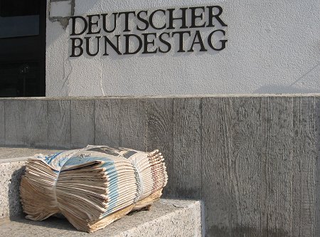 Ein abgepackter Zeitungsstapel liegt vor dem Schild "Deutscher Bundestag" auf einer Treppe.