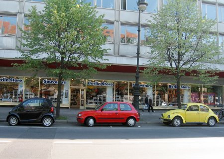 Drei Autos parken in einer Straße hintereinander: ein schwarzes, ein rotes und ein gelbes.