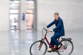 Marieluise Beck auf einem Fahrrad in der Halle des Marie-Elisabeth-Lüders-Hauses.