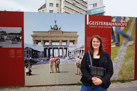 Kelly Hill vor einem Plakat der Ausstellung „Geisterbahnhöfe”