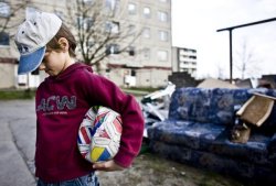 Kleiner Junge mit einem kaputten Ball unterm Arm kuckt traurig nach unten