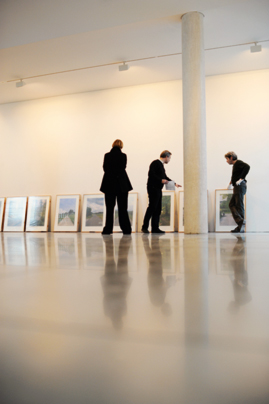 Bilder lehnen in der Ausstellungshalle des Kunst-Raums nebeneinander an der Wand, davor drei Personen