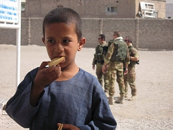 Foto: afghanisches Waisenkind isst einen Keks, im Hintergrund stehen NATO-Soldaten