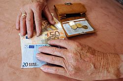 Hände eines alten Menschen, faltige Haende umgreifen Geldscheine.