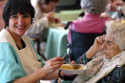 Eine alte Dame sitzt im Speisesaal eines Berliner Seniorenheimes und wird von einer Pflegerin gefüttert.
