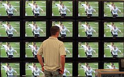 Mann steht vor Fersehwand, auf jedem Monitor läuft Fußball
