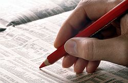 Eine Männerhand mit einem roten Stift geht die Aktiennotierungen im Börsenteil einer Zeitung durch