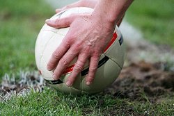 Hände halten einen Fussball auf einer Rasenfläche.