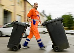 Ein Mitarbeiter der Müllabführ schiebt Container über die Straße.