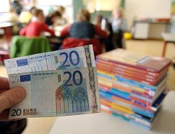 Eine Hand hält zwei 20-Euro-Geldscheine neben einen Stapel mit Schulbüchern im Klassenzimmer einer Schule, Klick vergrößert Bild