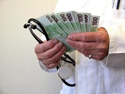 Ein Arzt im Kittel hält Gelscheine und ein Stetoskop in der Hand.