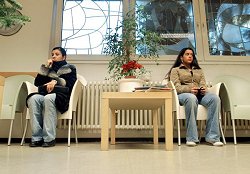 Wartezimmer der Praxis eines Arztes für Allgemeinmedizin: zwei jungen Frauen warten sitzend auf Stühlen.