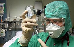 Mit Handschuhen, Schutzbrille und Atemfilter gegen eine Infektion geschützt, bereitet ein Arzt eine Injektion vor.