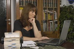 Eine Frau sitzt am Schreibtisch und schaut auf den Laptop. Sie macht die Buchführung.