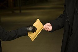 Eine Hand mit schwarzem Handschuh übergibt einen Umschlag an eine andere Hand.