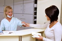 Eine Patientin übergibt der Arzthelferin ihre Krankenversicherungskarte.