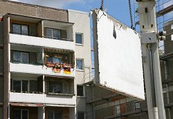 Wohnungen der Städtischen Wohnungsbau GmbH (SWB) Schönebeck werden gegenwärtig abgerissen. Im Hintergrund ist ein Balkon mit den Fahnen der DDR und der Bundesrepublik geschmückt.