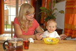 Eine Mutter hilft ihrem kleinen Sohn am Mittagstisch beim Essen.