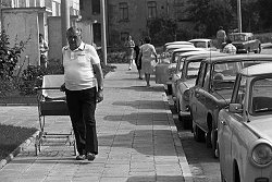 Ein alter Mann mit Kinderwagen im Neubaugebiet in der Lutherstadt Eisleben, 1983. Am Straßenrand sind PKW abgestellt, zumeist vom Typ Trabant.