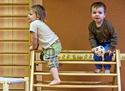 Zwei kleine Kinder klettern im Kindergarten auf einem Holzgerüst.